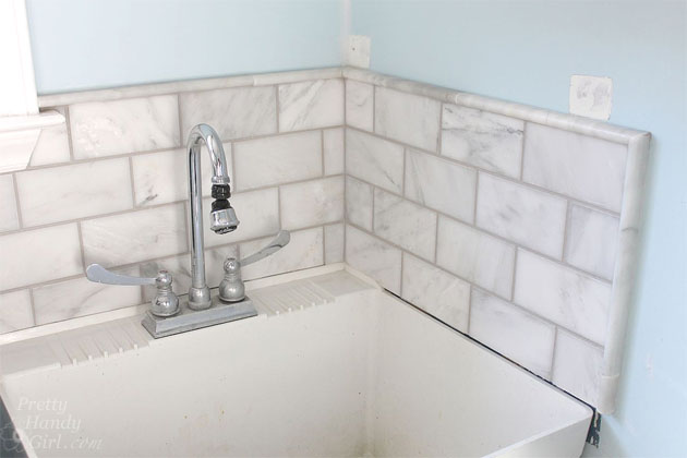 tiled and grouted marble subway tile backsplash around utility sink